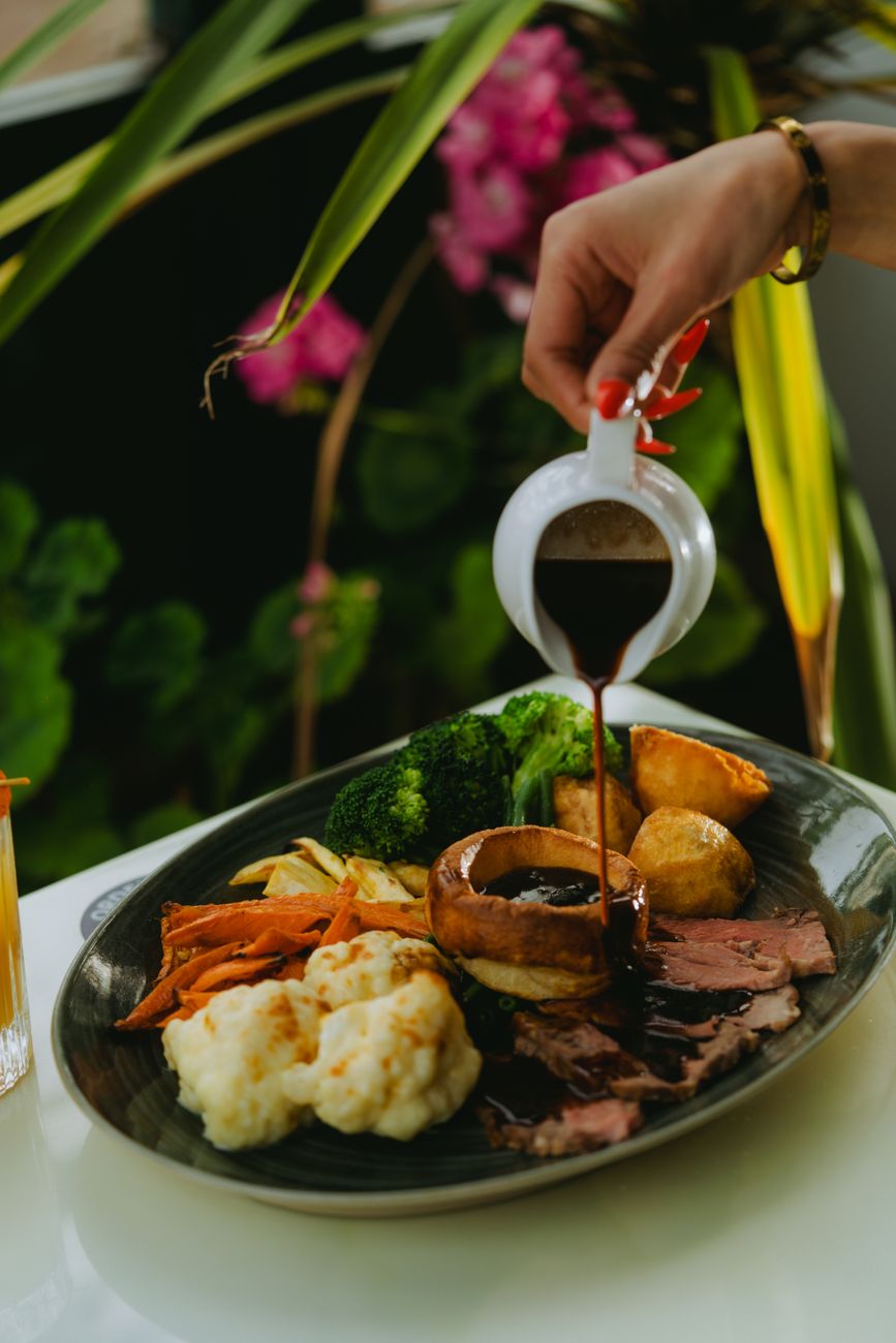 woman pouring sauce on meat and vegetables on a plate